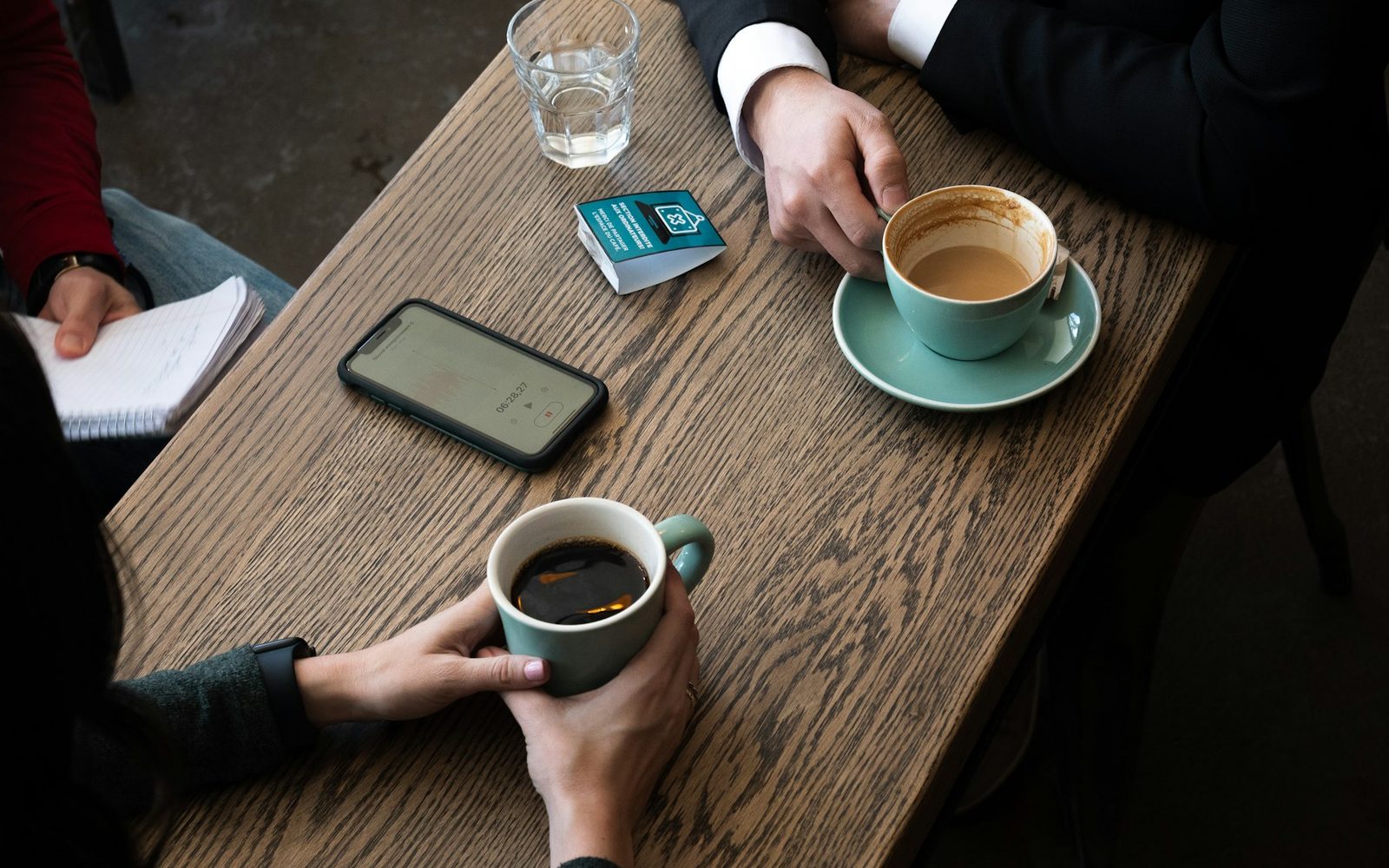 Zwei Personen an einem Holztisch mit Kaffee, Smartphone und Notizblock, von oben fotografiert